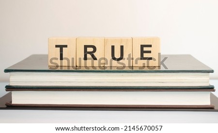 True - word written on wooden blocks. text is written in black letters and is reflected in the mirror surface of the table, blue background. business concept for your design
