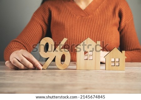 Female holding home model and sale percentage sign.