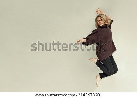 Blonde european girl with short hair in casual clothes jumping with inspirational expression. Active young woman having fun in a beige room. copy space