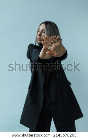 Young caucasian woman with short haircut shows stop gesture in the office. Female in black suit. The concept of a normalized work schedule