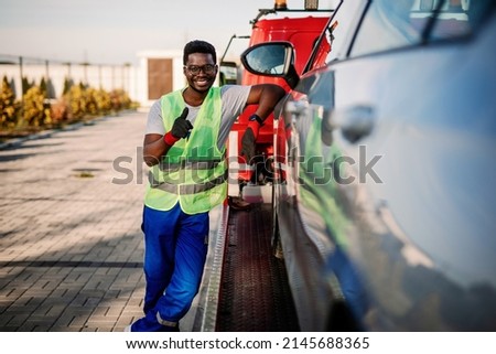 Portrait of handsome young African American man showing thumbs up while working in towing service on the road. Roadside assistance concept. Royalty-Free Stock Photo #2145688365