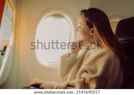 A beautiful girl sits in an airplane at the window and looks at the view. Tourist travel. Royalty-Free Stock Photo #2145690257