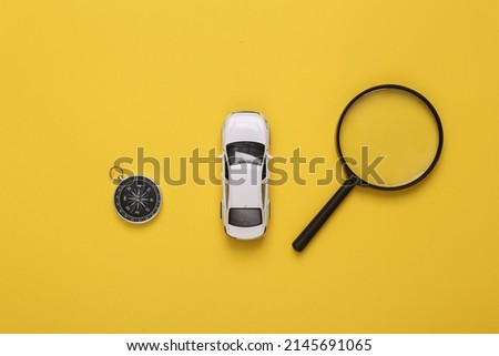 Travel concept. Toy car with compass and magnifying glasses on a yellow background. Top view