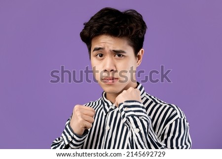 Power and Self Defence Concept. Headshot portrait of brave young Asian man ready to hit and fight, clenching fists to make or block punch isolated on purple violet studio background wall
