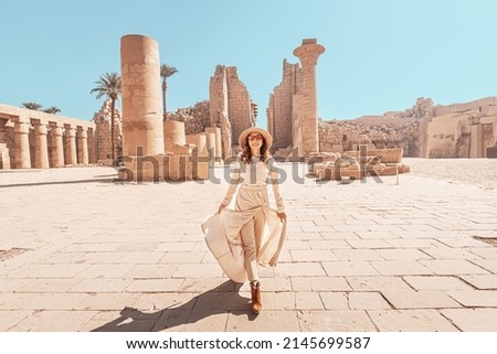 Happy woman traveler explores the ruins of the ancient Karnak temple in the heritage city of Luxor in Egypt. Giant row of columns with carved hieroglyph Royalty-Free Stock Photo #2145699587