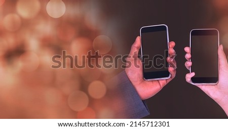 Composition of light circles over two diverse male and female hands holding smartphones. global communication and social networking concept digitally generated image.