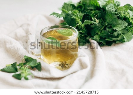 nettle tea. a cup with nettle tea next to a bunch of fresh nettles on a light background. medical herbal tea. Royalty-Free Stock Photo #2145728715