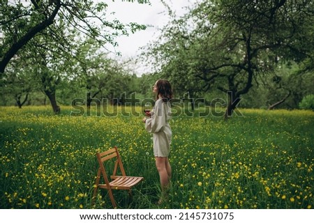 Several focus. Beautiful woman smells precious red wine with closed eyes in garden with blossomed flowers on background
