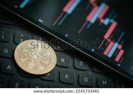 Golden Cardano (ADA) cryptocurrency coin with candle stick graph chart, laptop keyboard, and digital background. Royalty-Free Stock Photo #2145733481