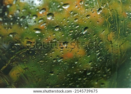Closeup of raindrops on a window with blurred colorful autumn foliage outside