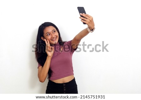 Cheerful young asian girl standing while doing selfie. Isolated on white background
