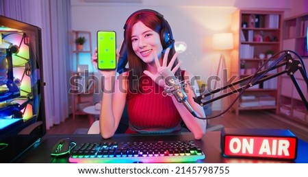 asian girl internet celebrity have a live stream with on air light sign and show app by the smartphone with green screen at home