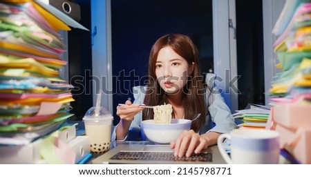 asian young businesswoman is eating instant noodles and tapioca ball milk tea with laptop computer while overworking in office at night Royalty-Free Stock Photo #2145798771