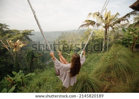 Rear view woman on a swing at vacation in Bali, Indonesia. Young girl traveler sitting on the swing in beautiful nature place in the mountains, tropical jungle view Royalty-Free Stock Photo #2145820189