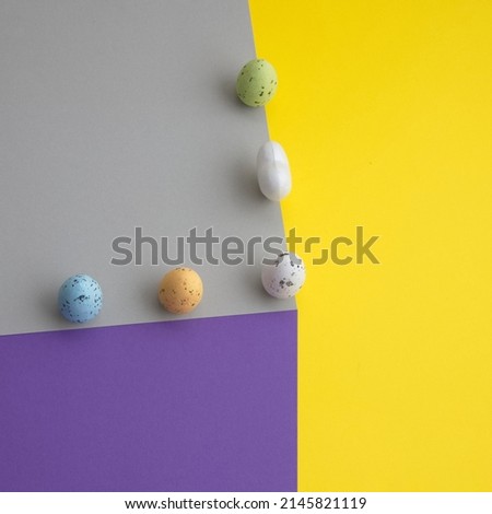 More colorful eggs and a white heart on a paper cube on a yellow background. Minimal Easter scene.