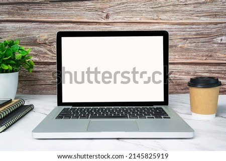 Laptop or notebook with blank screen, coffee, potted plant and notebooks.