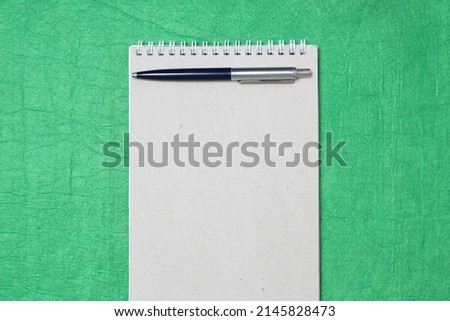 White and gray notepad sheet with spiral with pen against the background of green fabric. Concept of analysis, study, attentive work. Stock photo with empty place for your text and design.