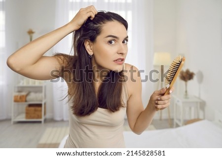 Portrait of woman in 20s 30s looking at her reflection with horrified nervous expression as she notices scalp dandruff, hair loss signs and receding hairline problem after stress and using bad shampoo Royalty-Free Stock Photo #2145828581