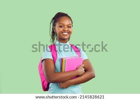 Smiling dark skinned female student with backpack and textbooks on light green background. Happy girl with pink backpack on her shoulders and with colorful textbooks in hands looks at camera. Banner. Royalty-Free Stock Photo #2145828621
