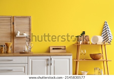Modern shelving unit with dishware and kitchen counter near yellow wall Royalty-Free Stock Photo #2145830577