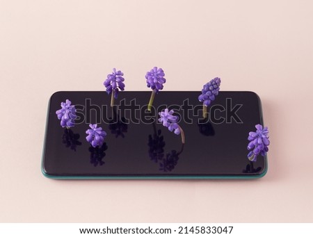 A phone with purple flowers growing from the screen. Soft pink background. Minimalist idea. Green Environment to Love and Care.