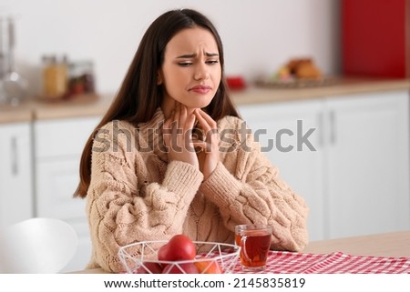 Young woman suffering from sore throat at table in kitchen Royalty-Free Stock Photo #2145835819