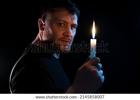 A man with a burning candle in his hand in the dark.