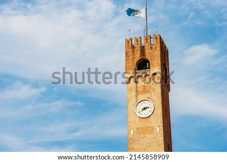 Close-up of the ancient medieval Civic Tower in Treviso Downtown, 1218, with the flag of the city. Town square called Piazza dei Signori, Veneto, Italy, Europe.