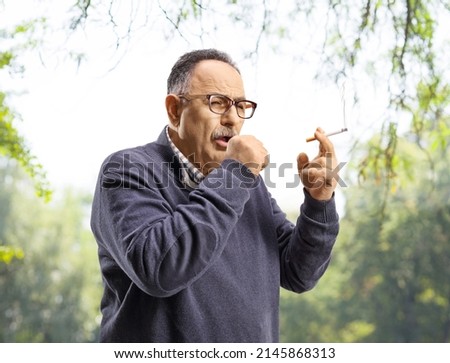 Mature man smoking and coughing outdoors in a park Royalty-Free Stock Photo #2145868313
