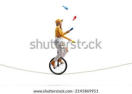 Young female riding a unicycle on a tightrope and juggling isolated on white background Royalty-Free Stock Photo #2145869951