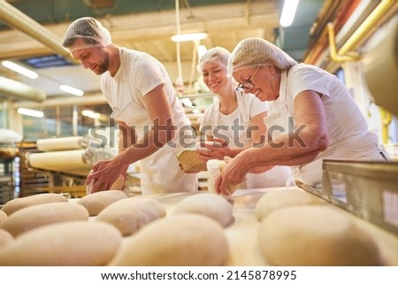 Senior woman as a baker with a team baking a loaf of bread in the family Royalty-Free Stock Photo #2145878995