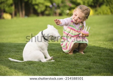 Young girl with birthday doughnut stroking dog in garden