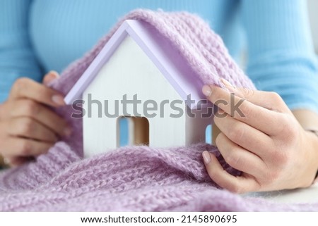 Close-up of woman cover house toy miniature with knitted scarf, symbol for heating system or cold snowy winter. Heating season, warm up, protect concept