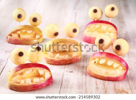 Spooky Halloween party favors or decorations made from fresh apples and dough in the form of open mouths lined with teeth topped with round googly eyes on a rustic table, creative country handicraft