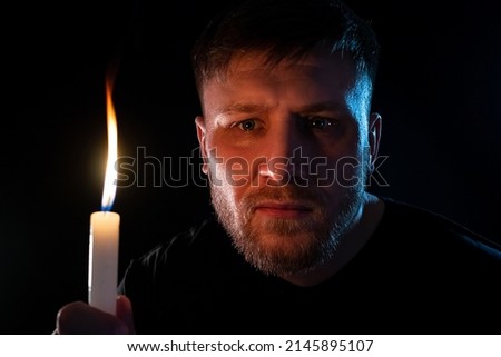 A man with a burning candle in his hand in the dark.