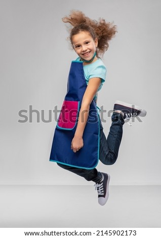 cooking, culinary and profession concept - happy smiling little girl in apron jumping over grey background