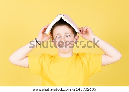 Boy holding a book on head and making funny face isolated on yellow background Royalty-Free Stock Photo #2145902685