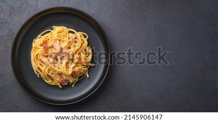 Linguini pasta with carbonara sauce on a dark background. Carbonara sauce made of bacon, parmesan, eggs, cream and pepper. Italian food. Royalty-Free Stock Photo #2145906147