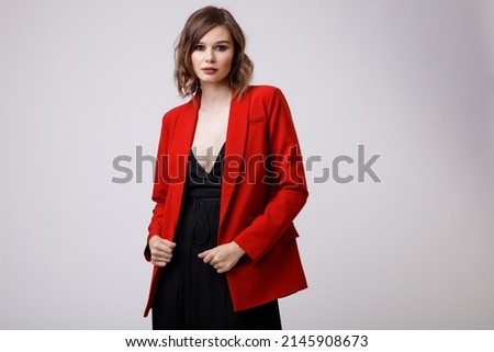 High fashion photo of a beautiful elegant young woman in a pretty black evening party dress with a deep neckline, red jacket posing on white background. Slim figure, hairstyle, studio shot. 