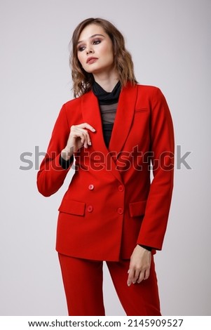 High fashion photo of a beautiful elegant young woman in a pretty red suit, jacket, pants, trousers, black blouse posing on white background. Slim figure, hairstyle, studio shot