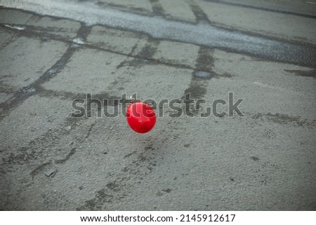 Red ball on background of asphalt. Abstract art. Sphere made of plastic. Inflatable balloon flies down street.