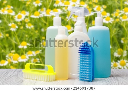 Plastic bottles of dishwashing liquid, glass and tile cleaner, detergent for microwave ovens and stoves, brushes on the blurred natural background. Washing and cleaning concept.