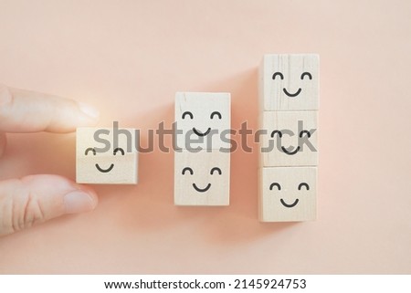 senior's hand hold smiling face icon on wood cube with orange background. Optimistic person or people feeling inside and service rating , team attitude, satisfaction concept in business
