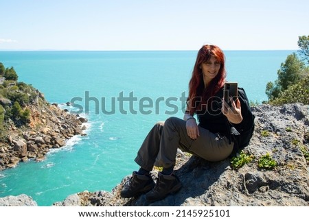 Woman trekker on the top of the mountain above the sea  takes a selfie with a mobile phone