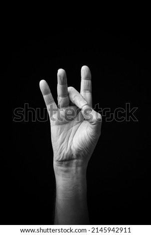 Dramatic black and white  image of a male hand fingerspelling the Ukrainian manual sign language letter 'Р', isolated against a dark background.