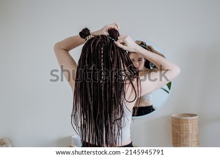 a girl with afro-braids straightens her hair in front of a mirror