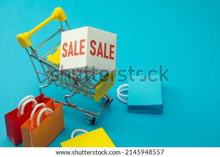 Sale promotion discount season in department store or e-commerce online web shopping concept. SALE paper box in supermarket trolley and colorful shopping bags on blue background copy space.