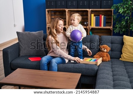 Mother and son playing with ball sitting on sofa at home