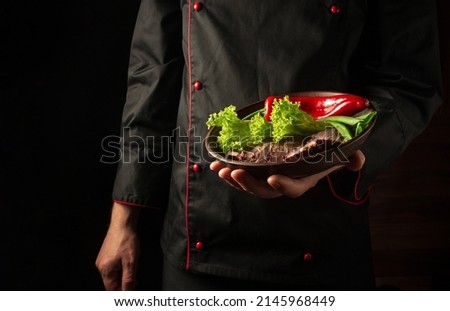 In the chef hand is a plate with chopped meat and vegetables. Food preparation concept on dark background. Asian cuisine