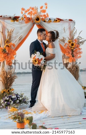 Loving couple at an international wedding at sunset. Beautiful sophisticated bride of Asian appearance. Strong manly groom of Caucasian appearance. Mixed marriages Royalty-Free Stock Photo #2145977163